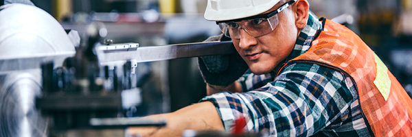 Manufacturing worker wears safety gear and operates a machine.